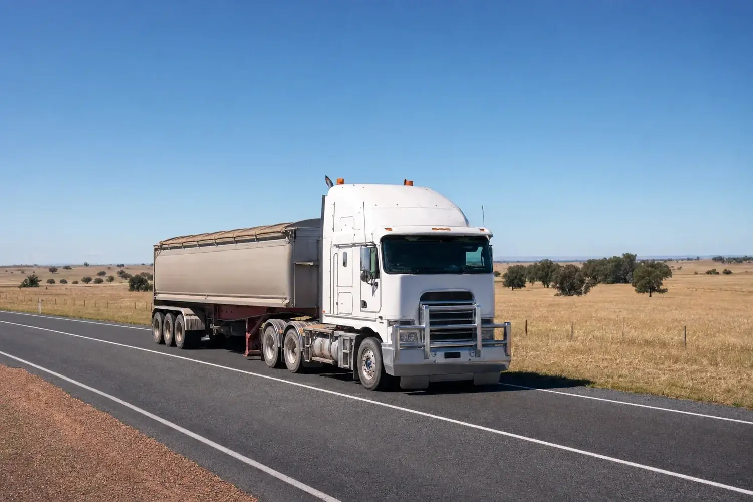 Prime mover hauling a grain trailer on a rural Australian highway through farmland