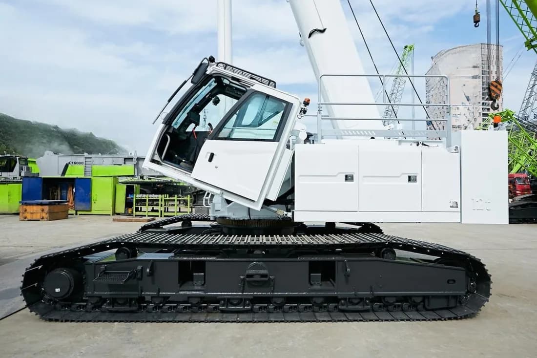 White crawler crane on steel tracks with the boom raised, parked on a hardstand at a crane yard