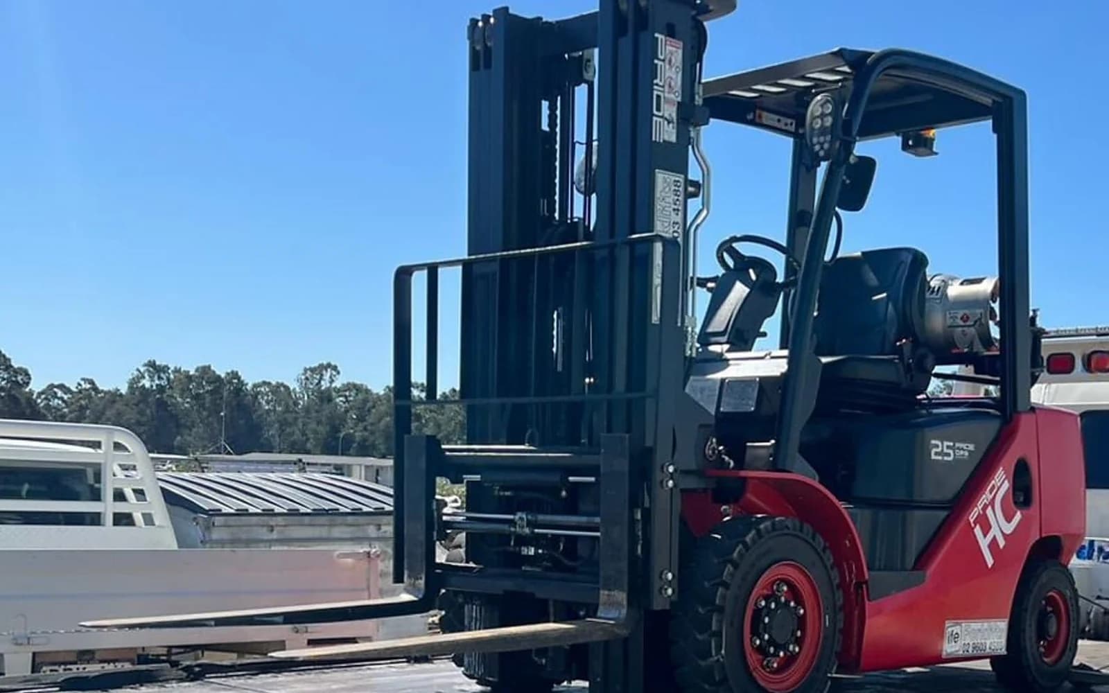 Red LPG counterbalance forklift with its mast raised, loaded on a truck tray at an Australian yard