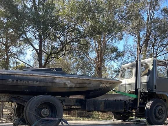 Fire-damaged rigid truck and burnt boat recovered on a tilt tray in Australian bushland
