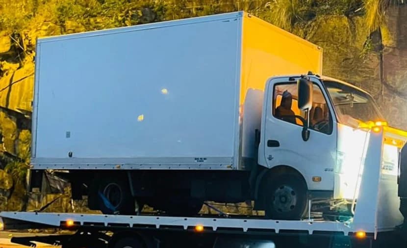 White light rigid pantech truck loaded on a tilt tray for recovery on an Australian road at dusk