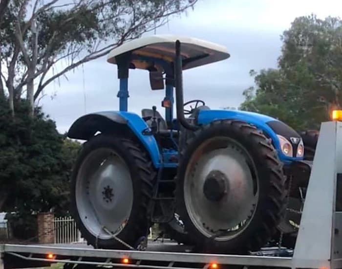 Blue tractor strapped to a tilt tray deck on an Australian rural road