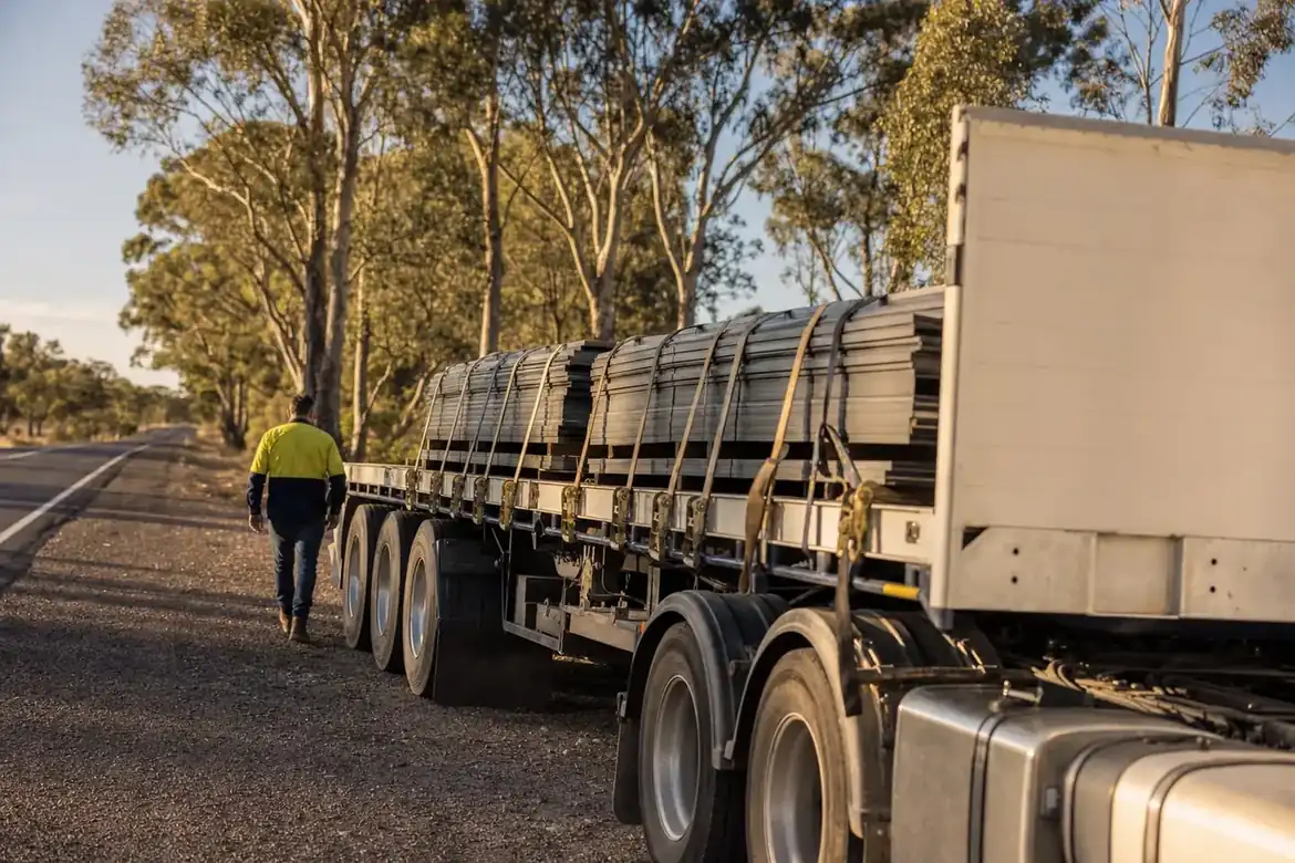 Transport worker inspecting a loaded flat-top semi-trailer parked at an Australian highway road stop with gum trees behind
