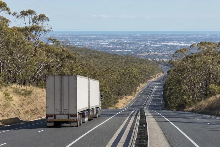 B-double keeping left on a divided freeway descending out of forested hills toward a flat plain in South Australia