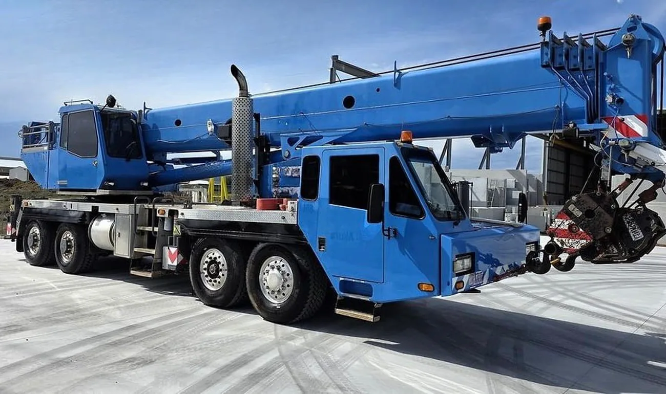 Blue all-terrain mobile slewing crane with the boom stowed, parked on a hardstand in Australia