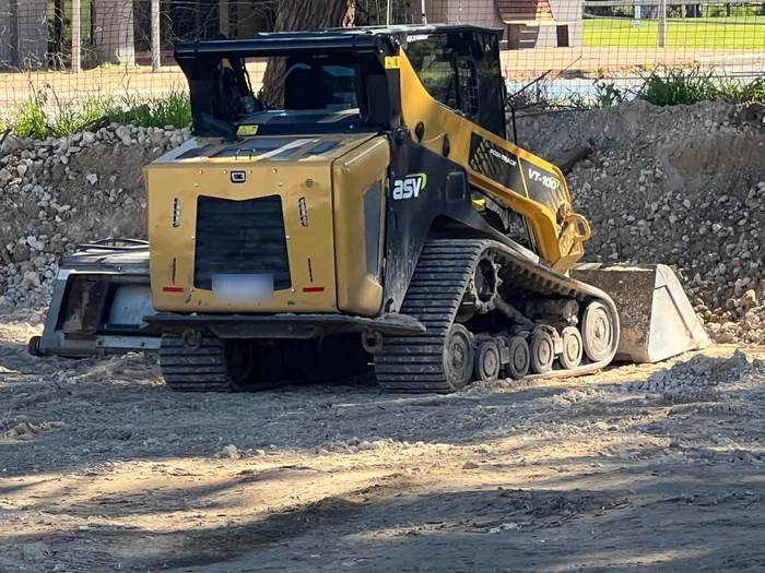 Yellow tracked compact loader with a levelling bar working across a rubble pad