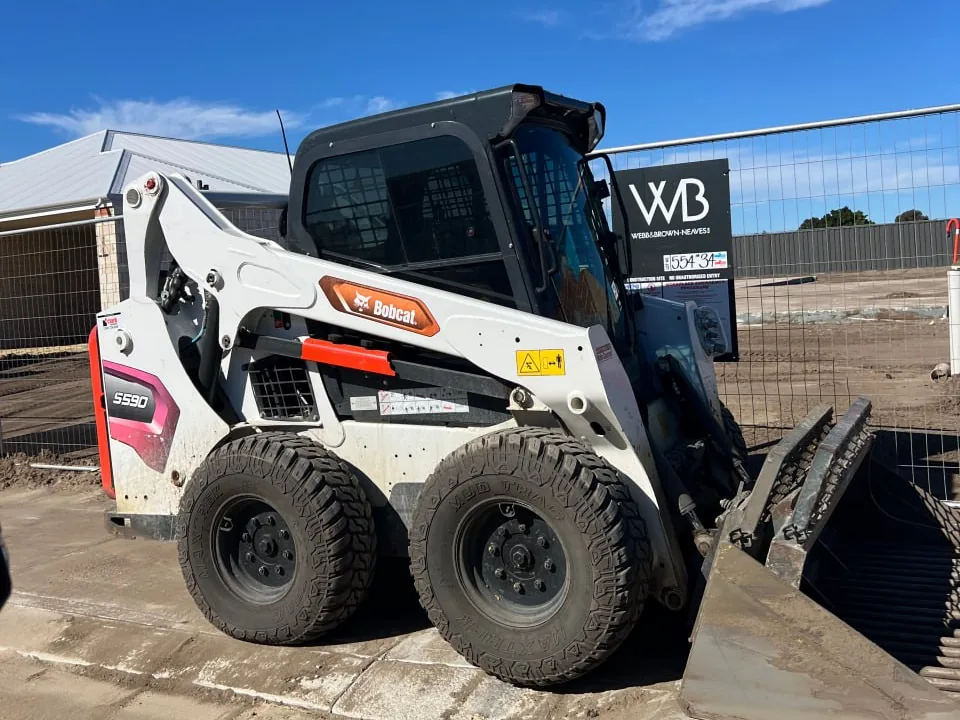 White Bobcat S590 skid steer parked on a concrete pad at a residential building site