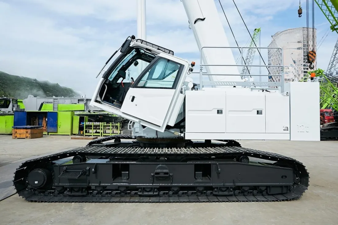 White crawler crane on steel tracks with the boom raised, parked on a hardstand at a crane yard