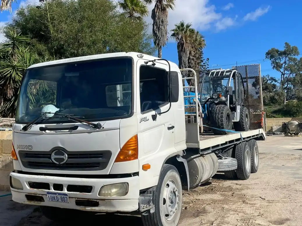 White Hino flatbed truck loaded with equipment in an Australian transport yard
