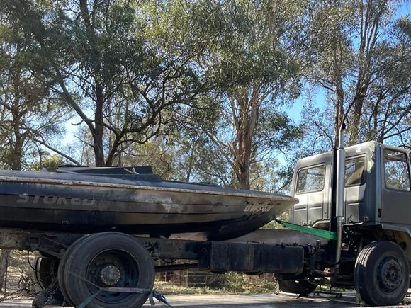 Fire-damaged rigid truck and burnt boat recovered on a tilt tray in Australian bushland