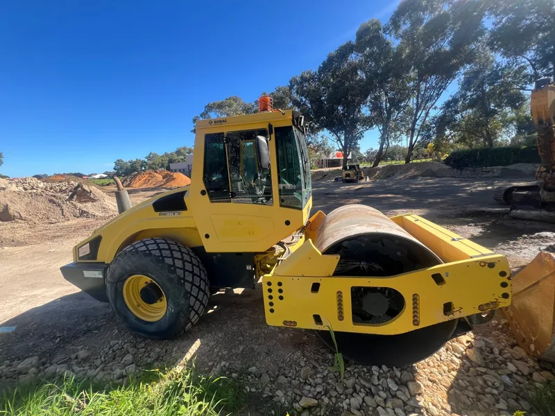Single drum roller standing on a cleared civil site with an excavator behind it