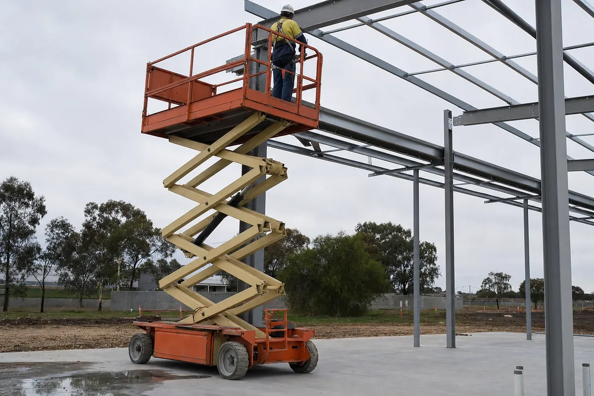 Scissor lift raised to working height beside a steel building frame on an Australian construction site