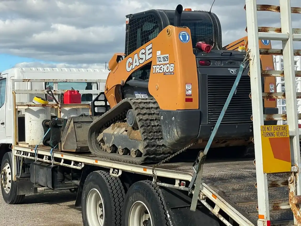 Truck carrying a tracked loader as freight on its tray at an Australian yard