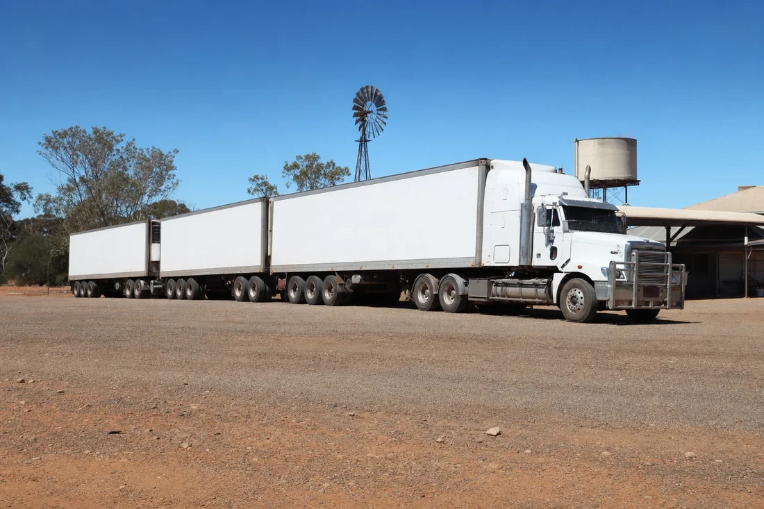 Triple road train parked on the gravel apron of an isolated highway roadhouse in arid South Australia
